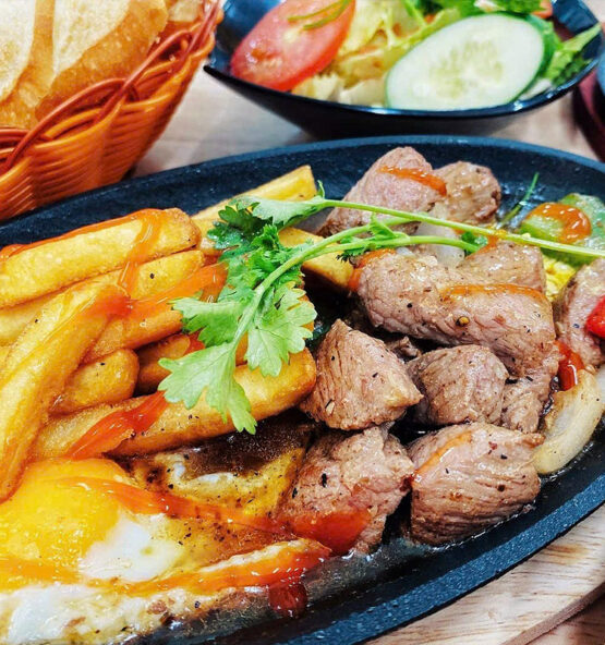 Bò lúc lắc trứng khoai tây tại Mộc Quán - Sự kết hợp hoàn hảo giữa vị ngọt mềm của thịt bò, độ béo ngậy của trứng và khoai tây vàng ruộm. Mỗi miếng bò được tẩm ướp đậm đà, khi chiên lên có lớp vỏ giòn tan bên ngoài, bên trong mềm ngọt. Cùng với trứng ốp la vàng ươm và khoai tây chiên giòn rụm, tạo nên một hương vị khó cưỡng, chắc chắn sẽ làm hài lòng mọi thực khách